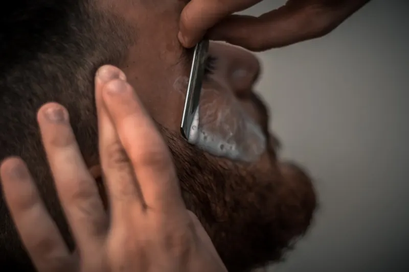 Barber shaping a full beard with a straight razor