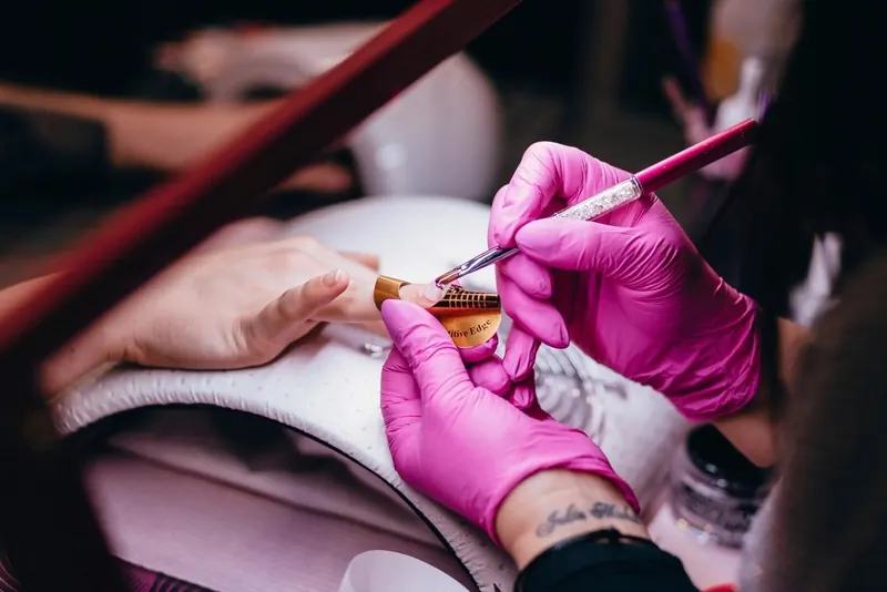 Nail technician in pink gloves painting a gel manicure